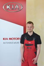 KFZ- Mechatroniker T.Schwamborn vor Kia Motors Logo Wand