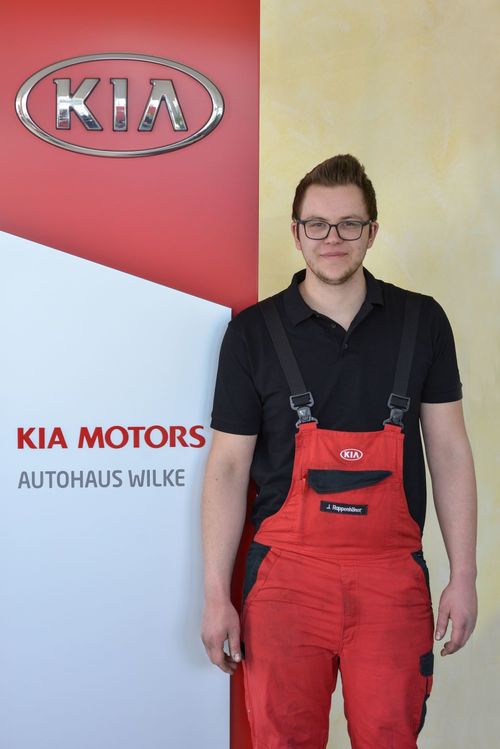KFZ- Mechatroniker J.Rappenhöner vor Kia Motors Logo Wand