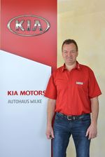 Inhaber Volker Wilke vor Kia Motors Logo Wand