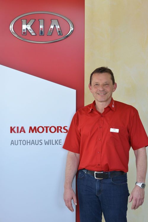 Verkäufer Thomas Lüsgen vor Kia Motors Logo Wand