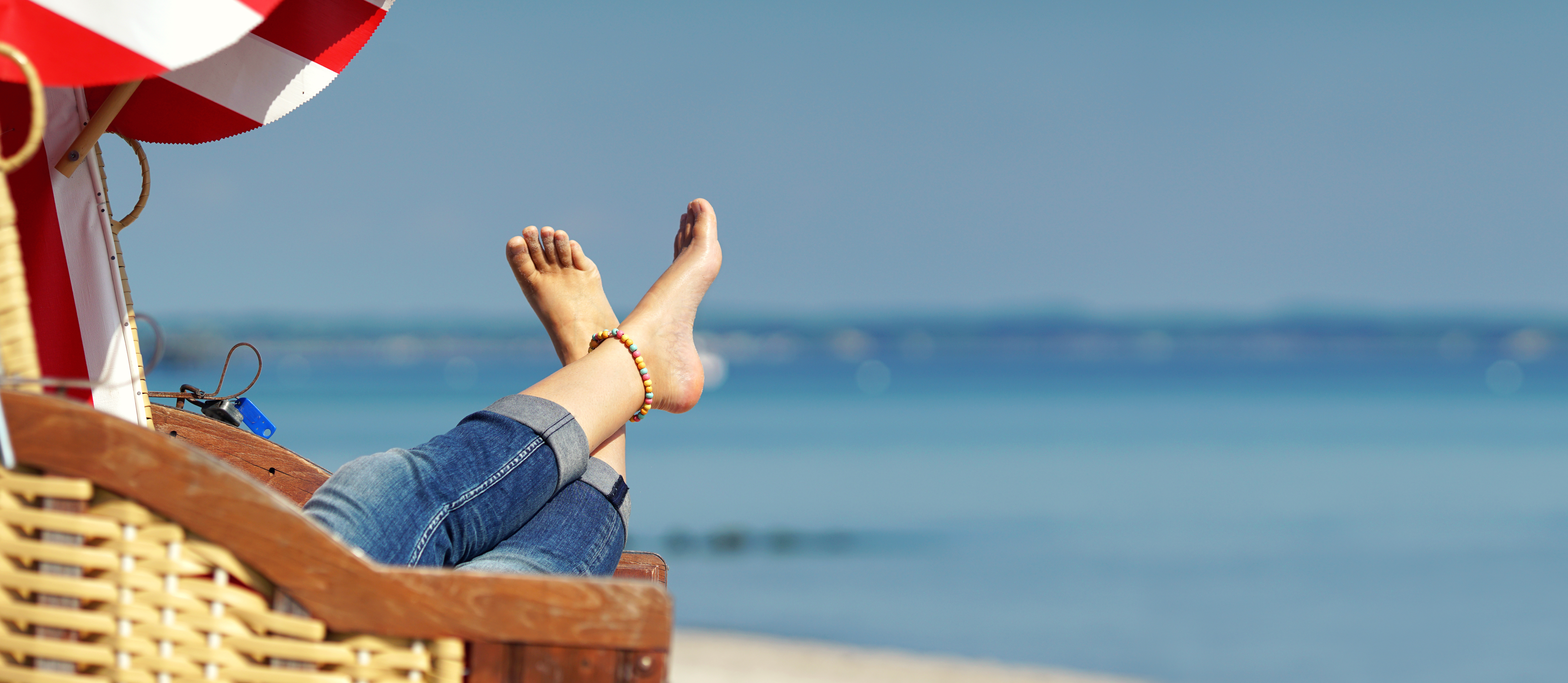 „Entspannung pur im Frühling: Eine Person genießt die wärmenden Sonnenstrahlen am Strand von Horumersiel, die Beine entspannt hochgelegt, während die frische Nordseeluft für pure Erholung sorgt. Perfekt für einen Frühlings-Kurzurlaub im Hotel Leuchtfeuer Horumersiel.“