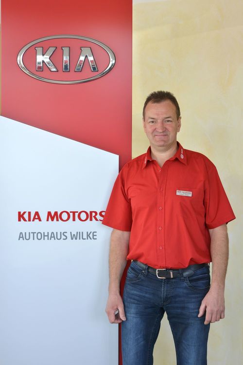 Bild Inhaber Volker Wilke vor Kia Motors Logo Wand