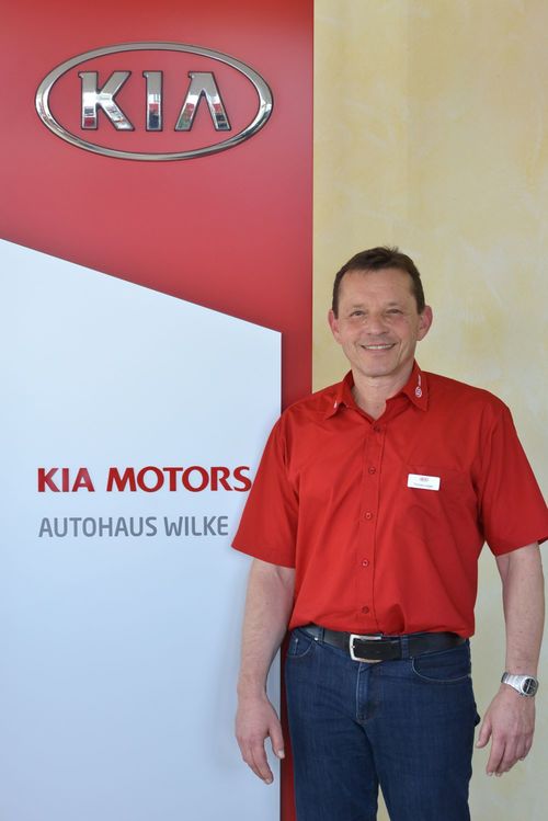 Bild Verk&auml;ufer Thomas L&uuml;sgen vor Kia Motors Logo Wand