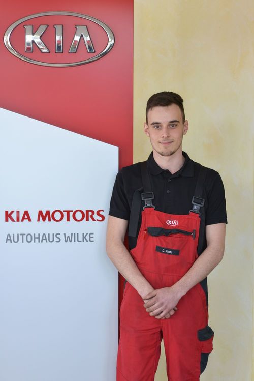 Bild Azubi KFZ- Mechatroniker D.Knak vor Kia Motors Logo Wand