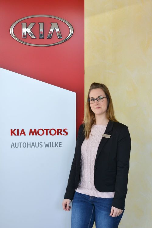 Bild Terminvergabe Dana Scholtis vor Kia Motors Logo Wand